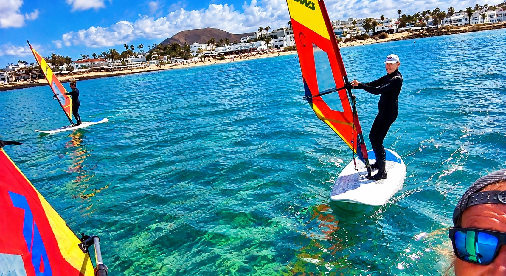Students windsurfing on the turquoise water of Corralejo bay during a NalooFuerte lesson