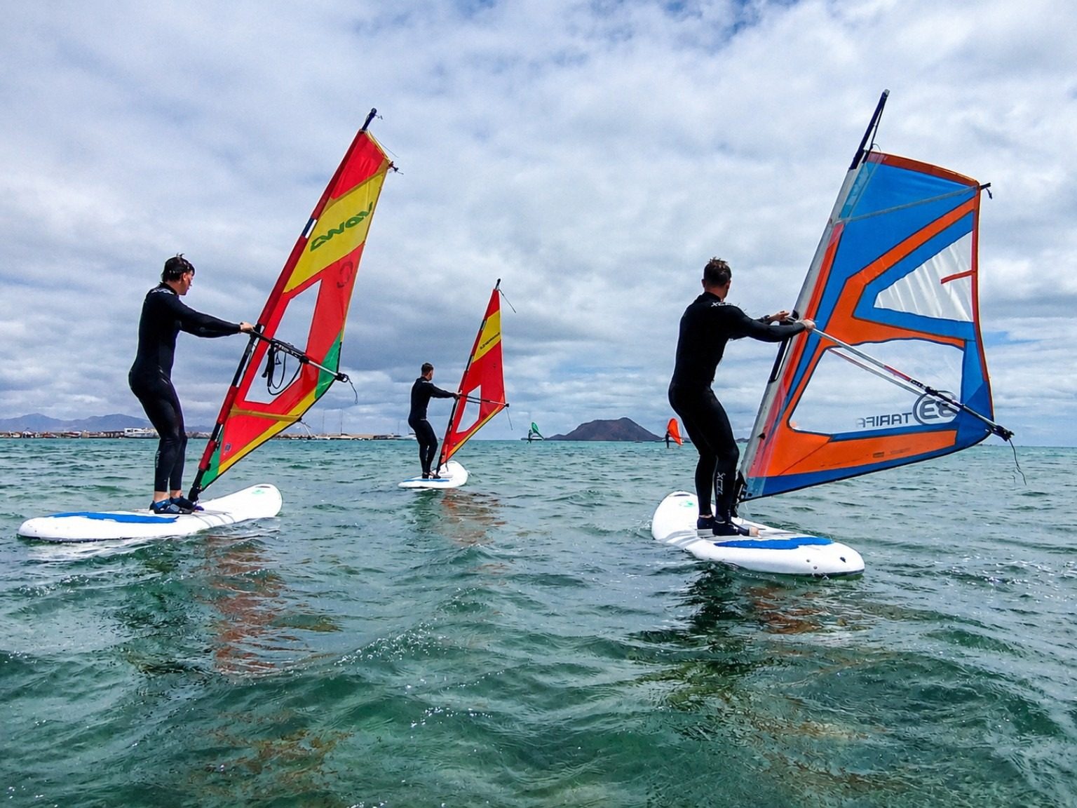 Three beginner windsurfers on the water during a NalooFuerte lesson in the bay of Corralejo, Fuerteventura