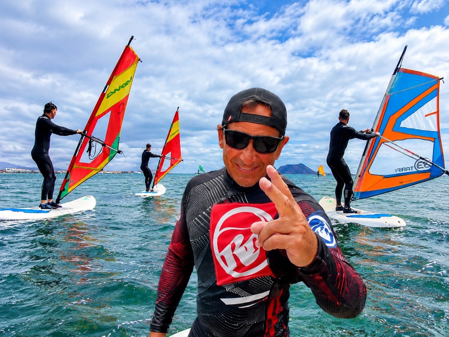 Paolo, NalooFuerte windsurf instructor, in the water with three students windsurfing behind him in the bay of Corralejo